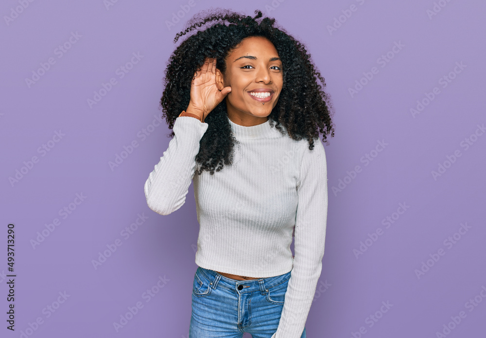 Young african american girl wearing casual clothes smiling with hand over ear listening an hearing to rumor or gossip. deafness concept. Young african american girl wearing casual clothes smiling with hand over ear listening an hearing to rumor or gossip. deafness concept.