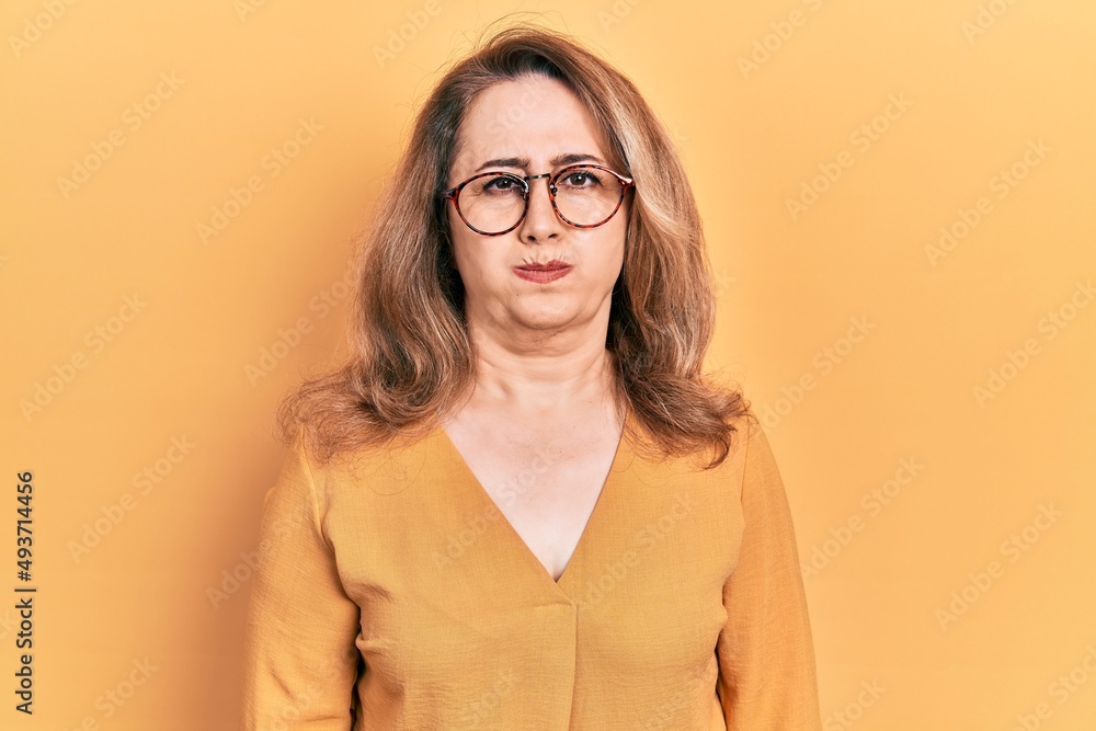 Middle age caucasian woman wearing casual clothes and glasses puffing cheeks with funny face. mouth inflated with air, crazy expression.