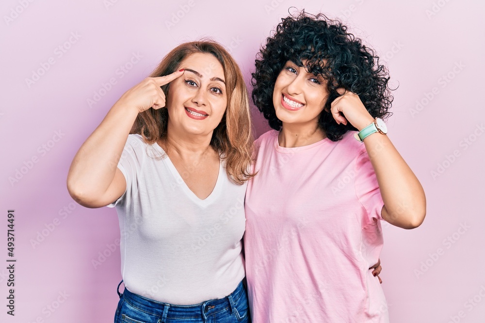 Middle east mother and daughter wearing casual clothes smiling pointing to head with one finger, great idea or thought, good memory