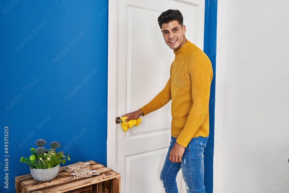 Young hispanic man smiling confident cleaning door knob at home