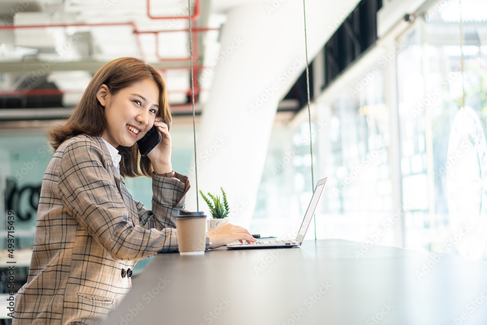 Young Asian woman using phone and laptop in coffee shop attractive young woman businesswoman smiling and talking on mobile phone in the office Young Asian woman using phone and laptop in coffee shop attractive young woman businesswoman smiling and talking on mobile phone in the office