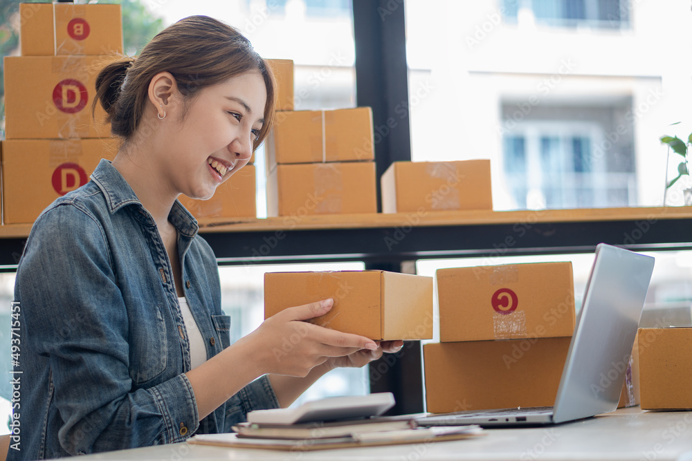 Portrait of a Small Business Startup, SME Owner, Female Entrepreneur Asian girl working on boxes and laptops, checking online orders to prepare boxes for sale to customers. Online SME business idea. Portrait of a Small Business Startup, SME Owner, Female Entrepreneur Asian girl working on boxes and laptops, checking online orders to prepare boxes for sale to customers. Online SME business idea.