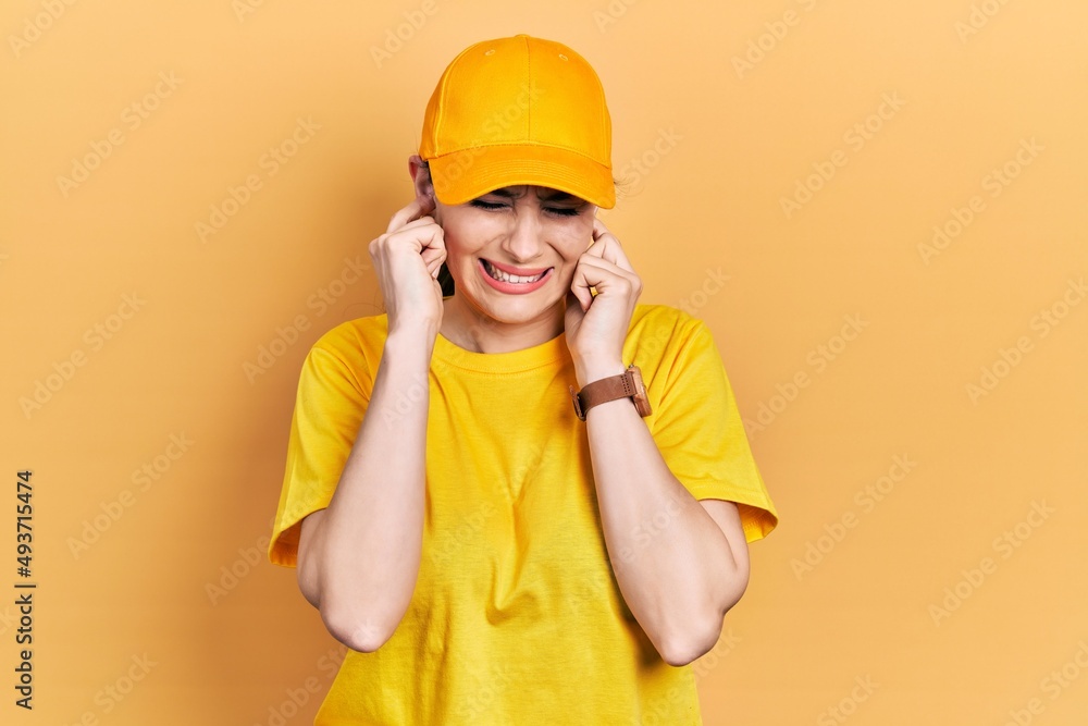 Young hispanic woman wearing delivery uniform and cap covering ears with fingers with annoyed expression for the noise of loud music. deaf concept. Young hispanic woman wearing delivery uniform and cap covering ears with fingers with annoyed expression for the noise of loud music. deaf concept.