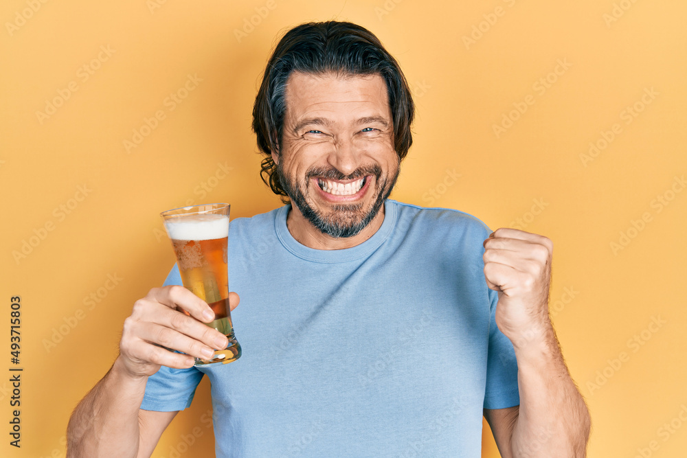 Middle age caucasian man drinking a pint of beer screaming proud, celebrating victory and success very excited with raised arm Middle age caucasian man drinking a pint of beer screaming proud, celebrating victory and success very excited with raised arm