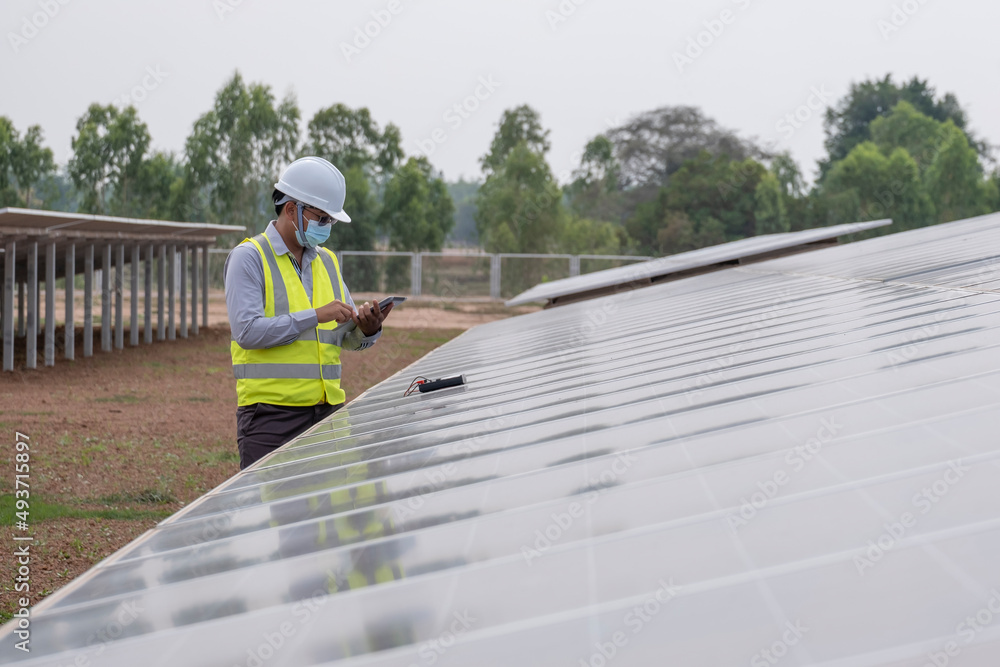 A young Asian engineer wearing a helmet and white mask checks the cleanliness of solar panels. renewable energy concept