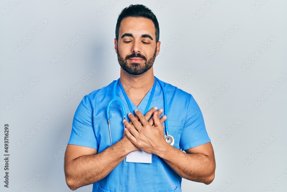 © Krakenimages.com - Handsome hispanic man with beard wearing doctor uniform smiling with hands on chest with closed eyes and grateful gesture on face. health concept. © Krakenimages.com - Handsome hispanic man with beard wearing doctor uniform smiling with hands on chest with closed eyes and grateful gesture on face. health concept.