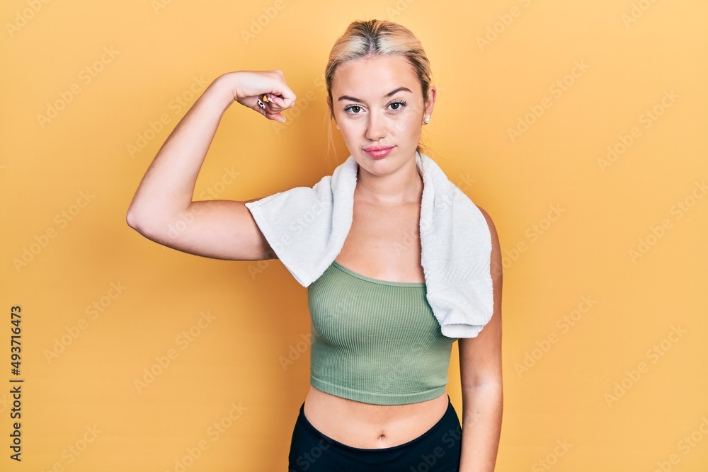 Young blonde girl wearing sportswear and towel strong person showing arm muscle, confident and proud of power Young blonde girl wearing sportswear and towel strong person showing arm muscle, confident and proud of power