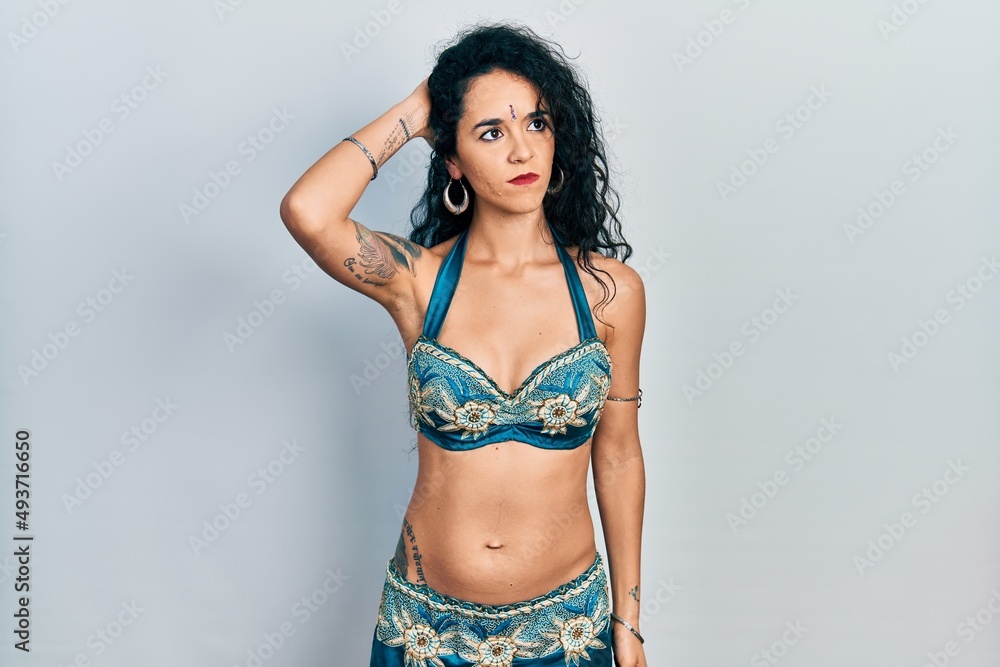 Fototapeta premium Young woman wearing bindi and traditional belly dance clothes confuse and wondering about question. uncertain with doubt, thinking with hand on head. pensive concept.