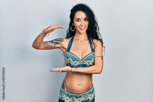 Young woman wearing bindi and traditional belly dance clothes gesturing with hands showing big and large size sign, measure symbol. smiling looking at the camera. measuring concept. © Krakenimages.com
