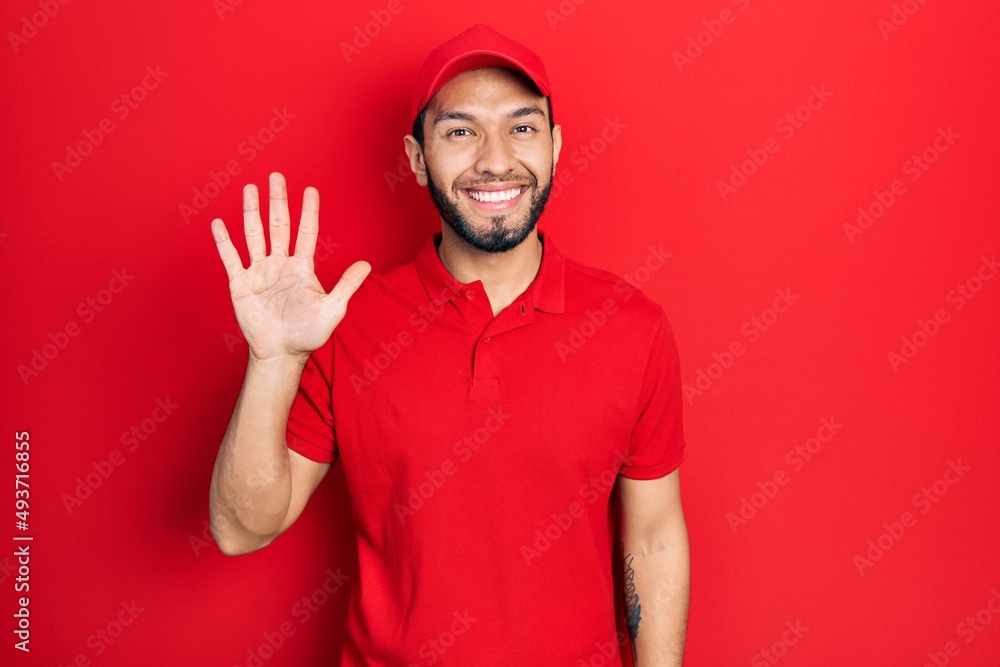 Hispanic man with beard wearing delivery uniform and cap showing and pointing up with fingers number five while smiling confident and happy. Hispanic man with beard wearing delivery uniform and cap showing and pointing up with fingers number five while smiling confident and happy.