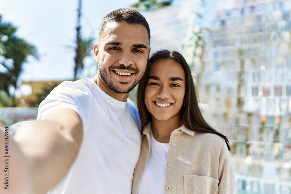 Fototapeta premium Young latin couple smiling happy and hugging making selfie by the camera at the city.