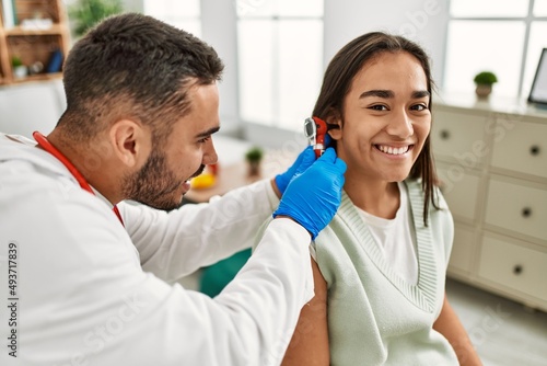 Doctor examining latin woman ear using otoscope at clinic.