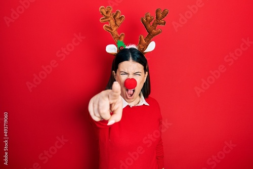 Young hispanic woman wearing deer christmas hat and red nose pointing displeased and frustrated to the camera, angry and furious with you