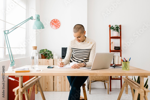 Front view of young adult trendy woman freelancer working on laptop computer at home. Stylish female studying online, using laptop software.
