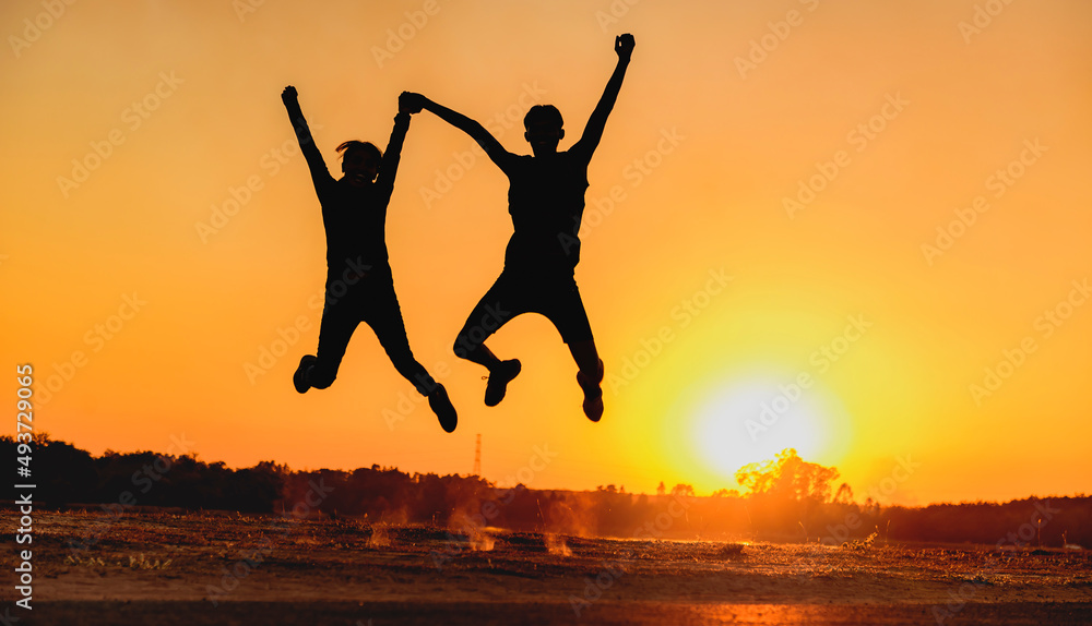 Male and female couple jumping happily at sunset with sun in the background, silhouette. Male and female couple jumping happily at sunset with sun in the background, silhouette.