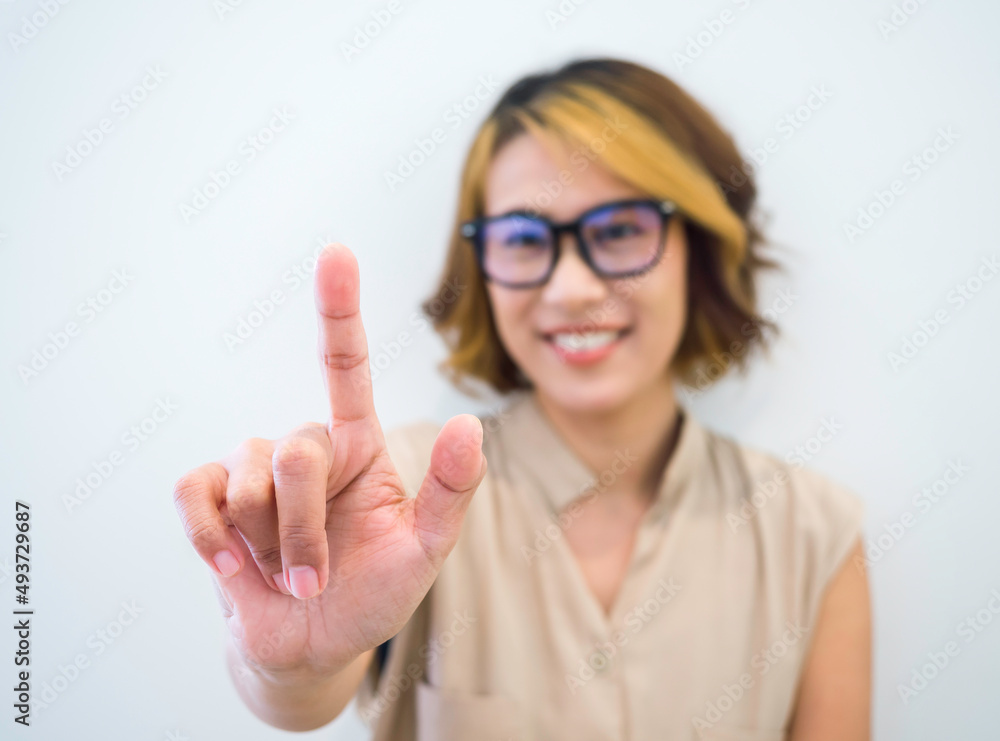 Closeup finger touch on virtual touch screen by happy smile Asian woman short hair wearing eye glasses with blue filter on white background. Hand point or press on empty space by businesswoman's hand.
