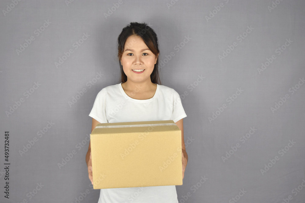 Asian woman smiling holding package box on grey background. Asian woman smiling holding package box on grey background.