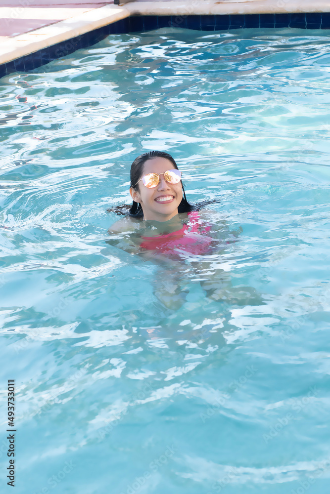 Young latin woman swimming in pool with sunglasses