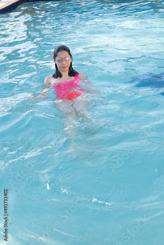 Young latin woman swimming in pool with sunglasses