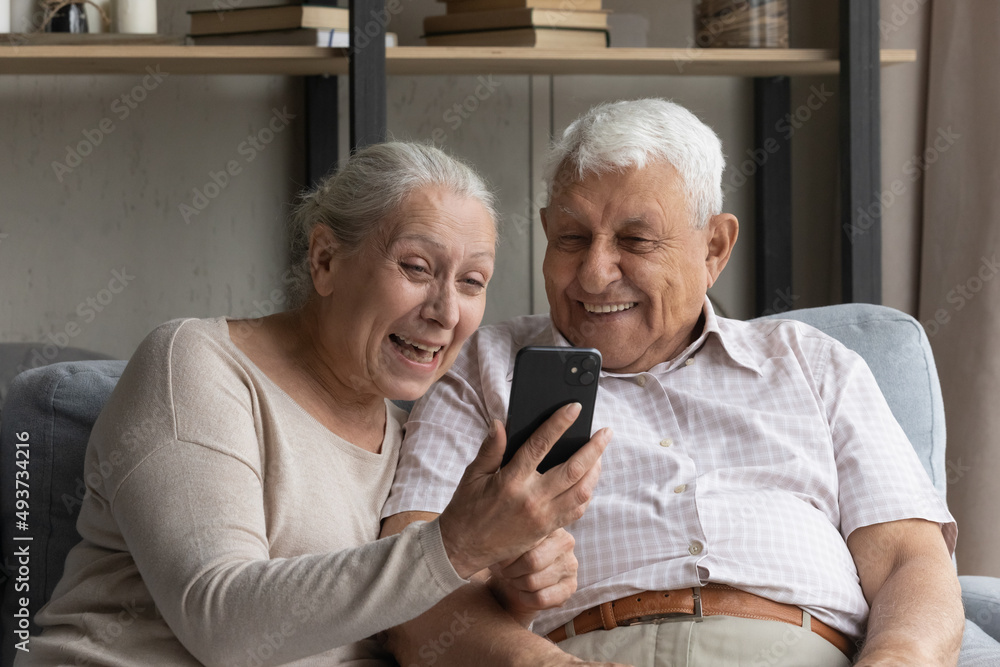 Happy older wife and husband laughing, have fun using modern smartphone, rest sit on sofa at home. Smiling senior couple read good news feel excited, get great offer, receive notice looking overjoyed Happy older wife and husband laughing, have fun using modern smartphone, rest sit on sofa at home. Smiling senior couple read good news feel excited, get great offer, receive notice looking overjoyed