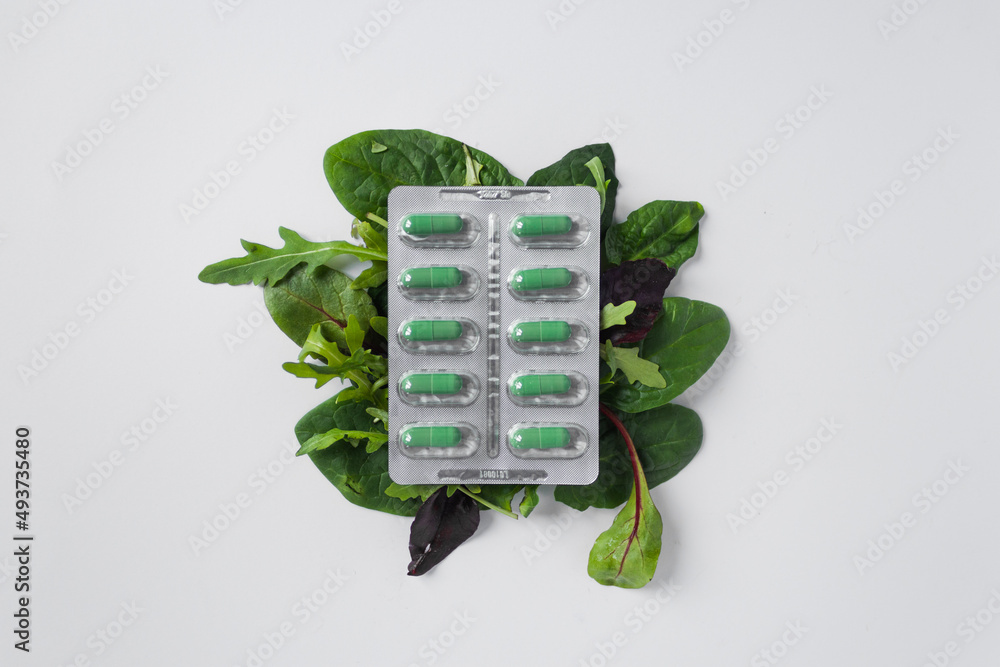 Silver blister with diet supplements in green capsules on the green leaves of arugula and lettuce. Health care concept. - obrazy, fototapety, plakaty 