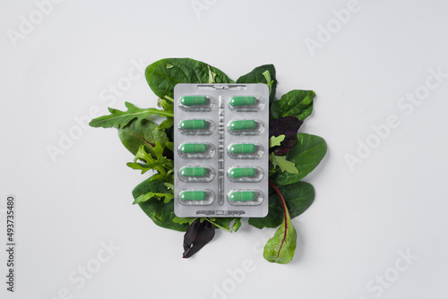 Obraz na plátne Silver blister with diet supplements in green capsules on the green leaves of arugula and lettuce