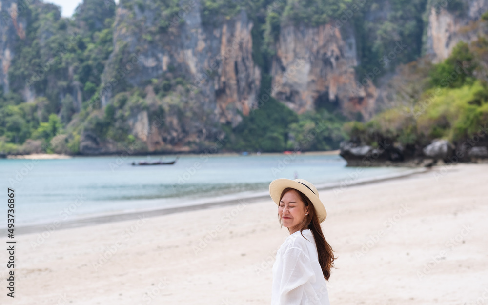 Portrait image of a happy young woman strolling on the beach with the sea and blue sky background