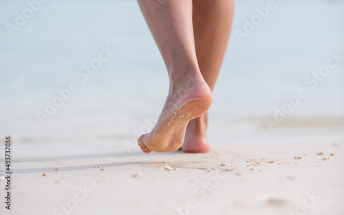 Closeup image of woman with barefoot while walking on the white beach and the sea