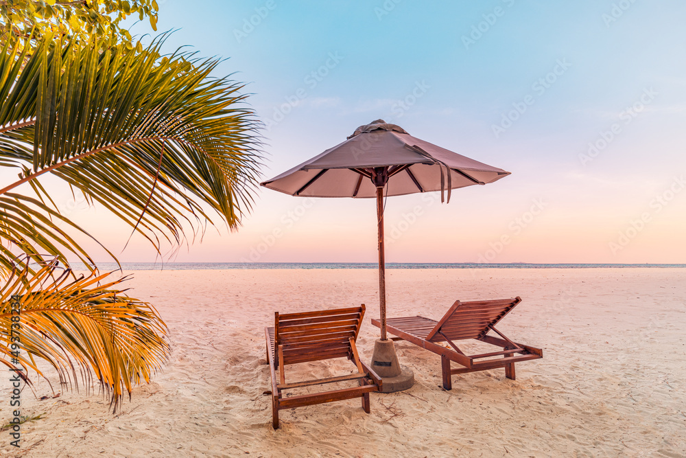 Perfect tropical sunset scenery, two sun beds, loungers, umbrella under palm tree. White sand, sea view with horizon, colorful twilight sky, calmness and relaxation. Inspirational beach resort hotel