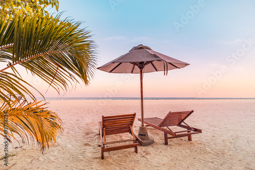Perfect tropical sunset scenery  two sun beds  loungers  umbrella under palm tree. White sand  sea view with horizon  colorful twilight sky  calmness and relaxation. Inspirational beach resort hotel