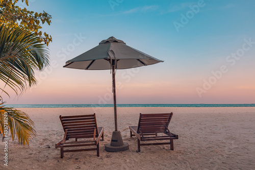 Perfect tropical sunset scenery, two sun beds, loungers, umbrella under palm tree. White sand, sea view with horizon, colorful twilight sky, calmness and relaxation. Inspirational beach resort hotel