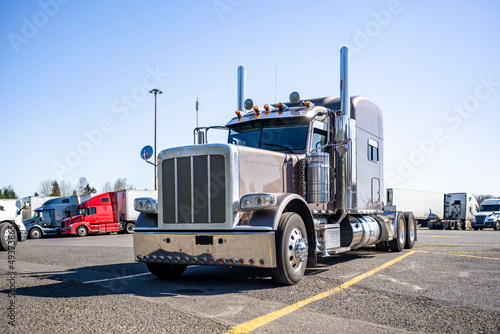 Coffee with milk big rig classic stylish semi truck tractor with extended cab and chrome parts standing along on truck stop parking lot with another semi trucks and trailers