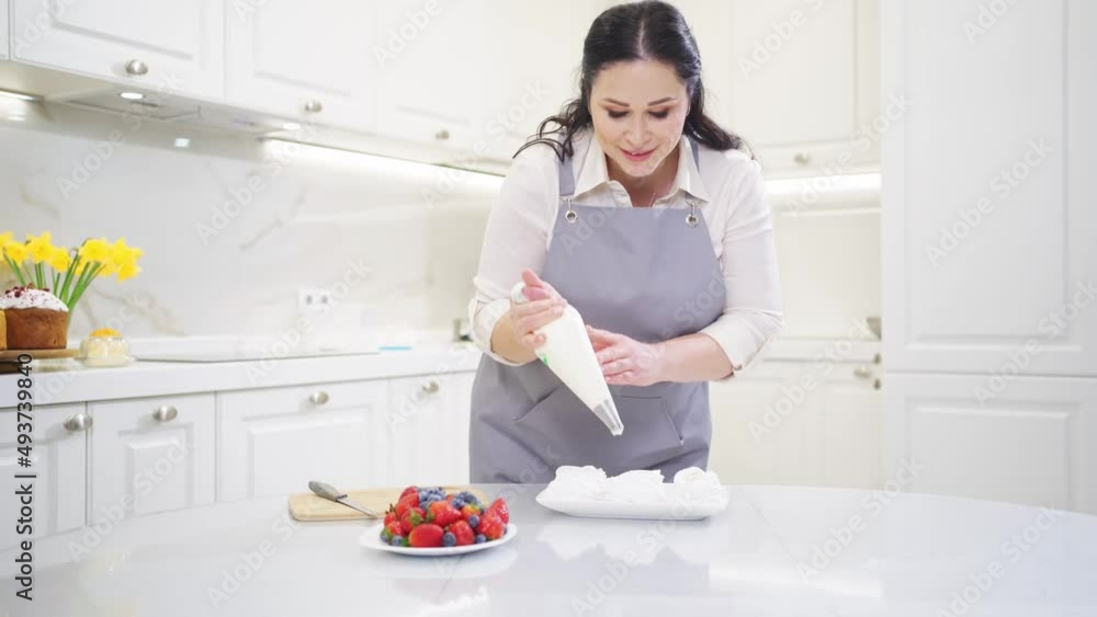 a female chef adds cream from a pastry bag to Anna Pavlova cakes in the kitchen. a female chef adds cream from a pastry bag to Anna Pavlova cakes in the kitchen.