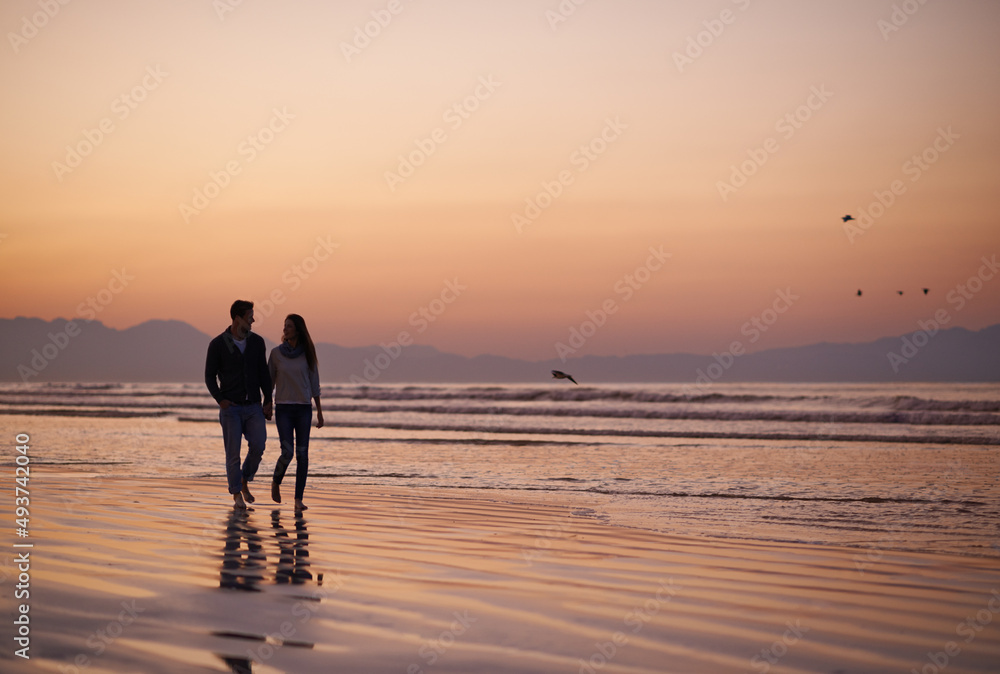 Theres nothing like young love. Silhouette of a young couple enjoying a romantic walk on the beach.