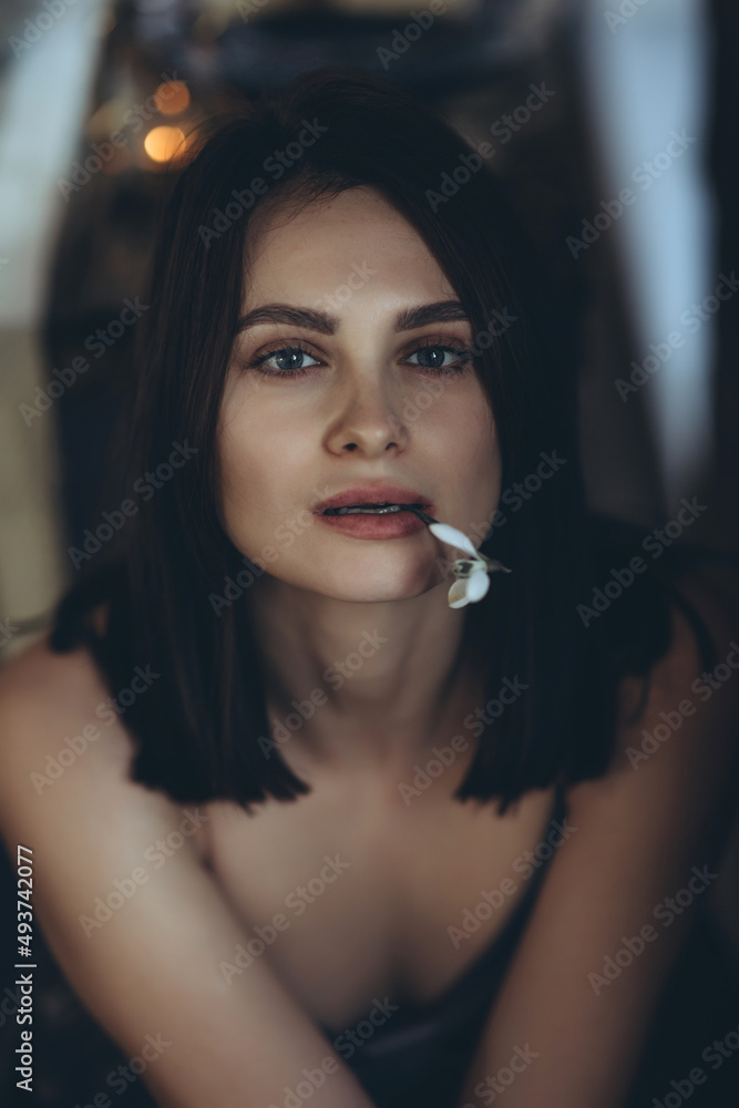 Fototapeta premium Portrait of a woman with a flower. A beautiful girl holds a snowdrop flower near her face. High quality photo