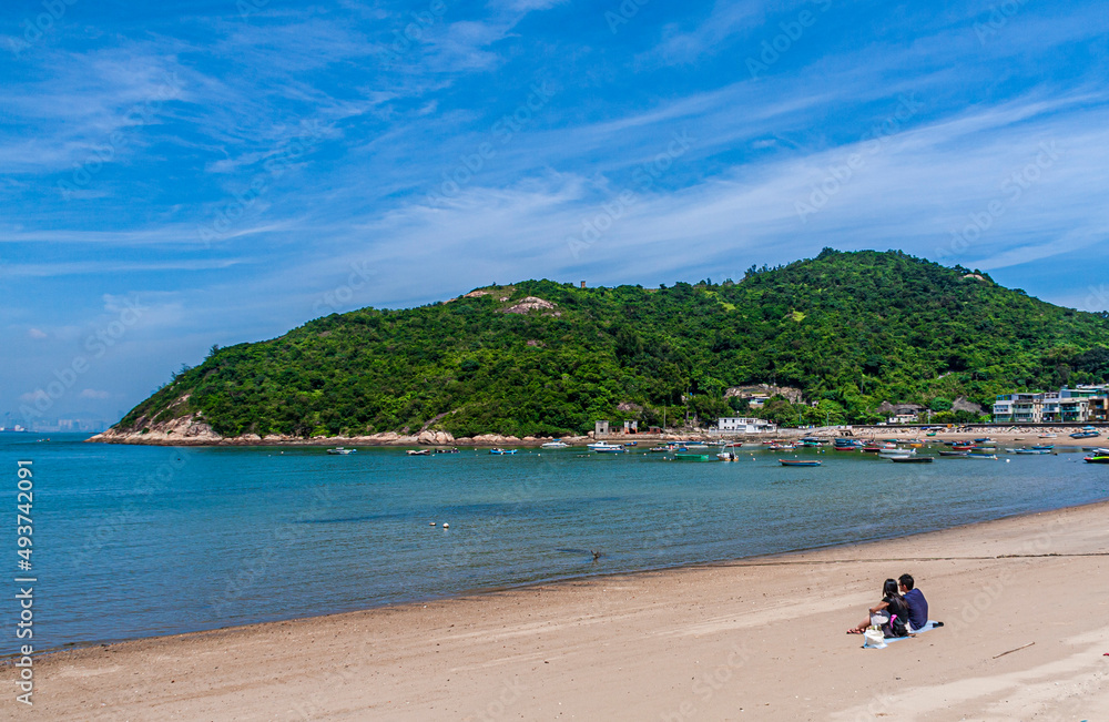 A couple sit on the beach watching a beautiful sea under blue sky on a sunny day in Hong Kong Peng Chau Island