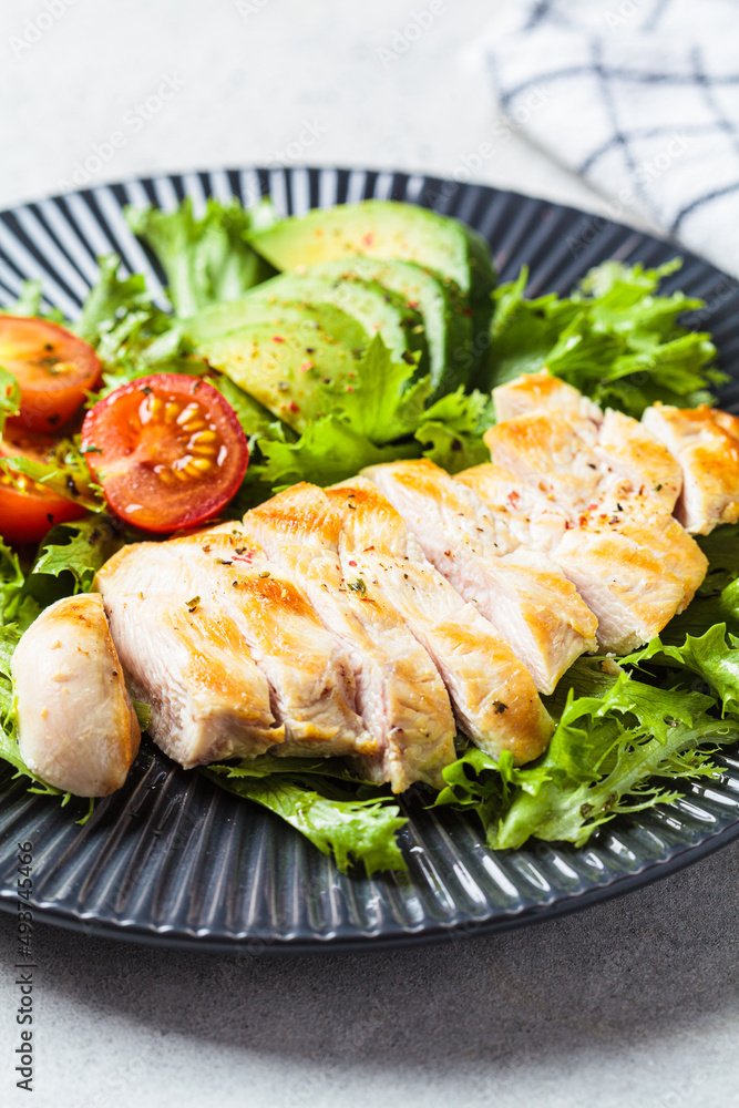 Grilled chicken breast salad with avocado and cherry tomatoes on gray plate. Healthy diet food concept.