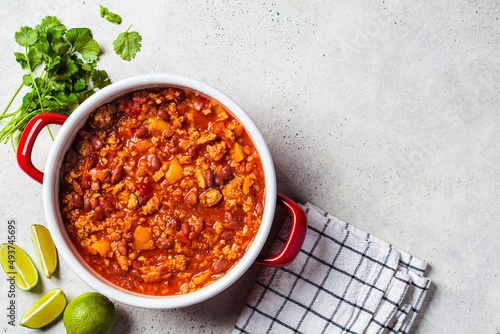 Vegan chili con carne with vegetables and beans in tomato sauce in a red saucepan. Mexican food concept.