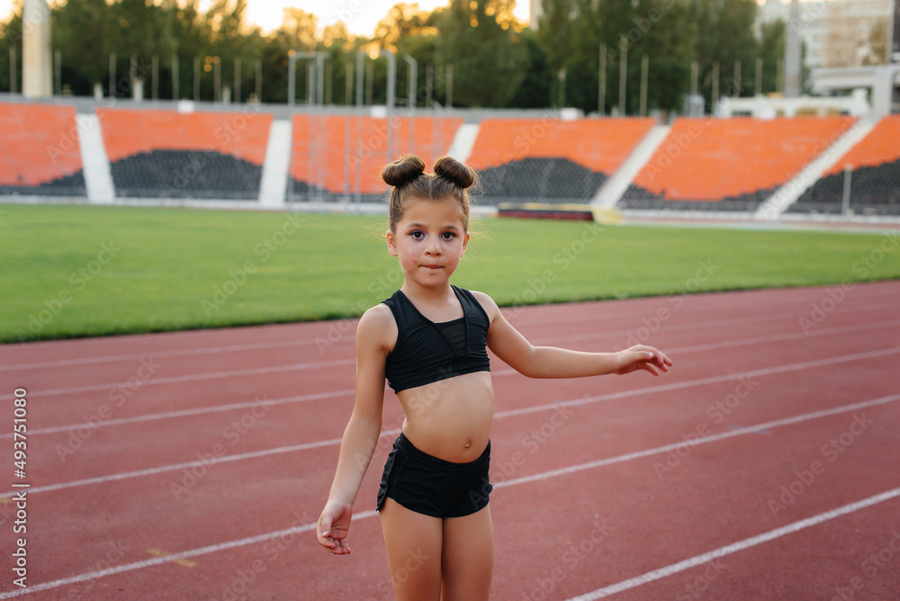 Obraz premium The girl is engaged in warm-up exercises and exercises in gymnastics and acrobatics in the summer at the stadium during sunset. Healthy lifestyle, sports training.