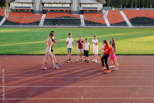 A large group of children, boys and girls, warm up and train under the guidance of a coach at the stadium during sunset. A healthy lifestyle.