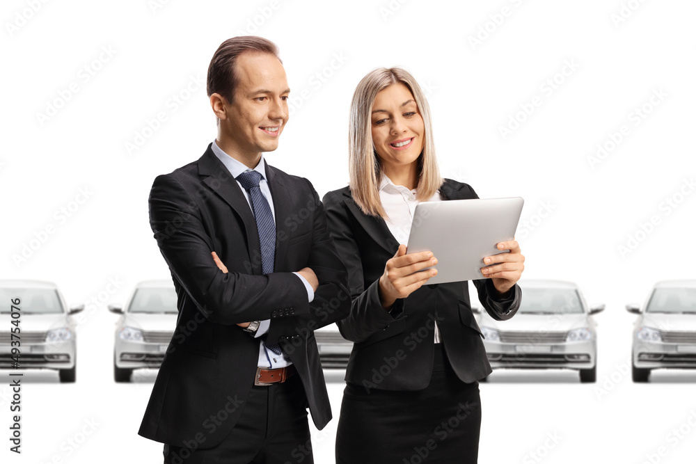 Woman showing a tablet to a businessman in front of new silver cars Woman showing a tablet to a businessman in front of new silver cars
