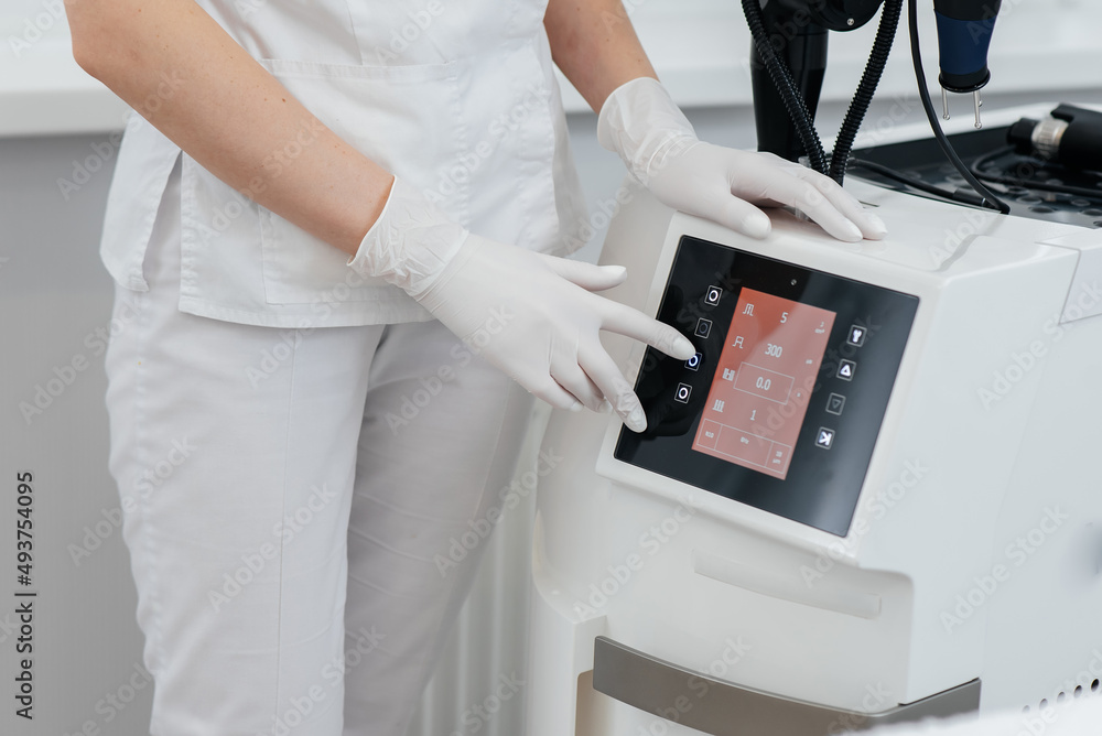 The cosmetologist's hand adjusts a modern laser in a beauty salon close-up. Laser pulses cleanse the skin. Hardware cosmetology. The process of photothermolysis, warming the skin. The cosmetologist's hand adjusts a modern laser in a beauty salon close-up. Laser pulses cleanse the skin. Hardware cosmetology. The process of photothermolysis, warming the skin.