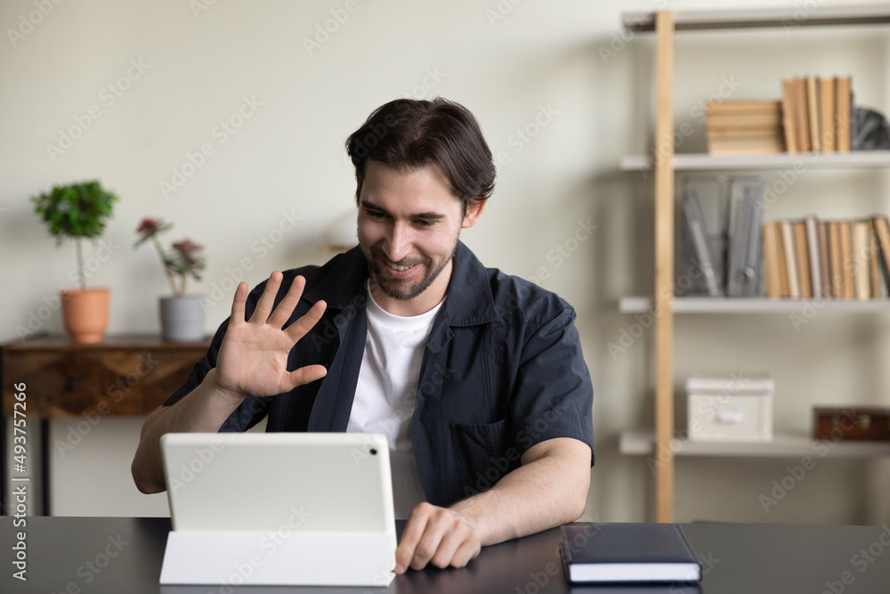 Fototapeta premium Happy friendly freelance tablet user guy waving hand hello at gadget screen, making distant video call to client, customer, using portable pc for business communication at office workplace table