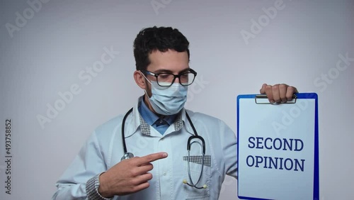 Healthcare professional worker in white medical scrubs and wearing surgical gloves and masks points holding a sign printed on paper with a relevant message for the society with text SECOND OPINION photo