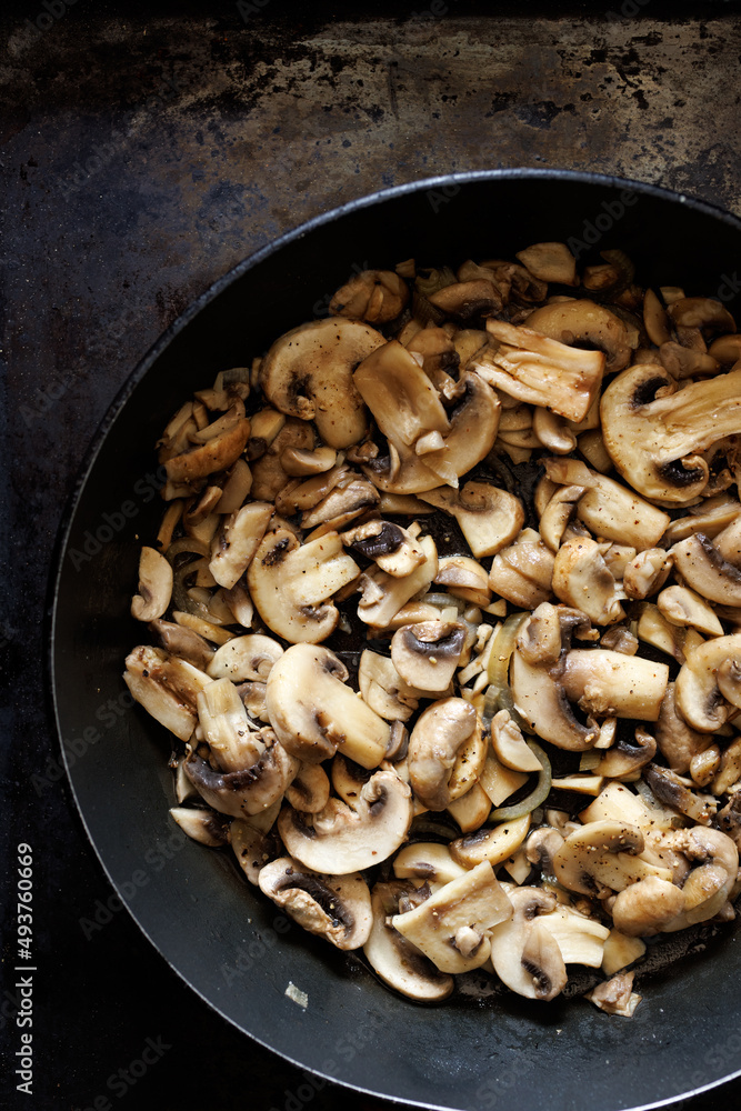 Fried sliced mushrooms, champignons in a pan on a dark background, close up view Fried sliced mushrooms, champignons in a pan on a dark background, close up view