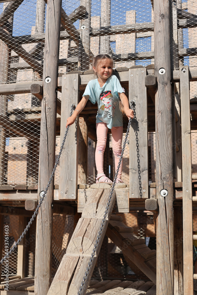 SAINT PETERSBURG, RUSSIA - JULY 6, 2021: A cute little girl playing in a playground made of natural wood.Child playing in the park. SAINT PETERSBURG, RUSSIA - JULY 6, 2021: A cute little girl playing in a playground made of natural wood.Child playing in the park.