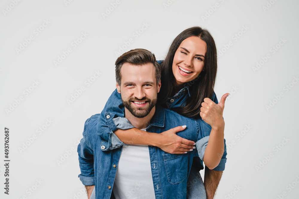 Young happy caucasian couple spouses girlfriend and boyfriend doing piggyback, dating, sharing love and passion showing thumb up isolated in white background Young happy caucasian couple spouses girlfriend and boyfriend doing piggyback, dating, sharing love and passion showing thumb up isolated in white background