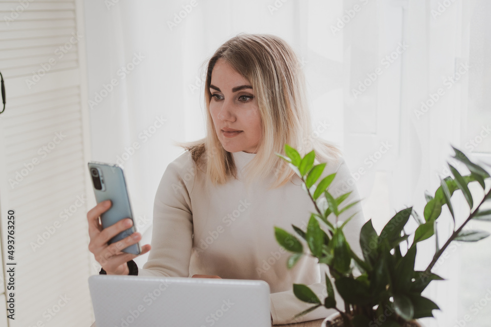 joyful charming woman using laptop and mobile phone smiling while sitting at the workplace joyful charming woman using laptop and mobile phone smiling while sitting at the workplace