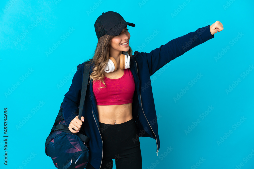 Young sport woman with sport bag isolated on blue background giving a thumbs up gesture Young sport woman with sport bag isolated on blue background giving a thumbs up gesture