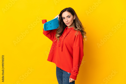 Young caucasian woman isolated on yellow background with a skate